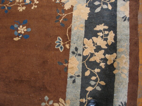 Brown rug with tan and blue floral designs and a wide striped border of gray and dark gray.