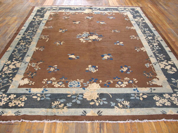 Brown floral rug featuring blue and cream motifs and a wide blue botanical border on hardwood floors.