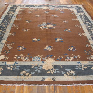A large brown rug with scattered blue and beige floral designs and complex blue and cream borders rests on wood planks.