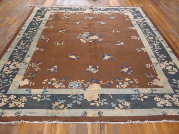 A large brown rug with scattered blue and beige floral designs and complex blue and cream borders rests on wood planks.