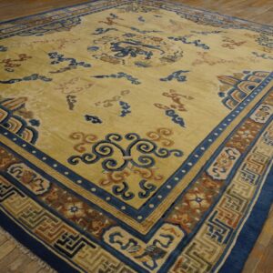 Large yellow rug with intricate blue, brown, and tan stylized patterns rests on a distressed wood floor.