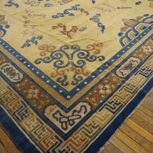 Pale yellow rug with blue, rust, and beige patterned borders rests on wide wood floorboards.