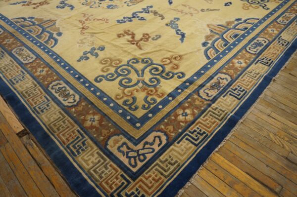Pale yellow rug with blue, rust, and beige patterned borders rests on wide wood floorboards.