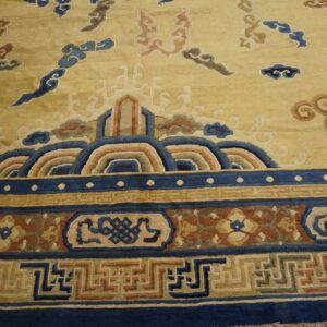Gold rug with complex blue, tan, and rust border featuring waves, Greek key, and floral designs.
