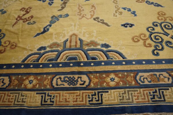 Gold rug with complex blue, tan, and rust border featuring waves, greek key, and floral designs.