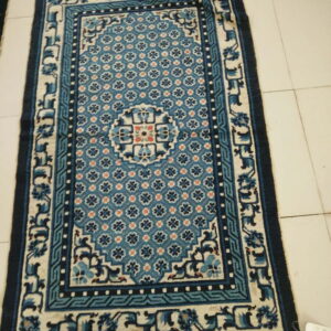 Low-pile rug in teal, navy, and cream colors, displaying a geometric pattern on light tile flooring.