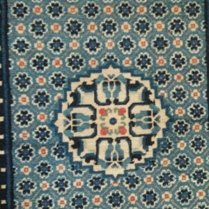 Low pile rug in blue, navy, and cream, featuring a geometric medallion and repeating floral trellis pattern.
