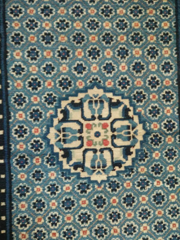 Low pile rug in blue, navy, and cream, featuring a geometric medallion and repeating floral trellis pattern.