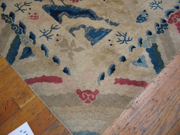 Beige rug corner featuring a scattered pattern of blue and red stylized motifs over hardwood floor.