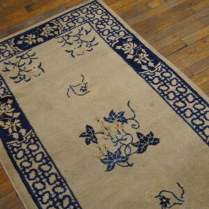 Low-pile beige rug with dark blue floral and geometric patterns shown on distressed hardwood flooring.