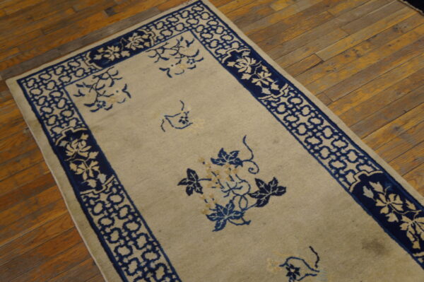Low-pile beige rug with dark blue floral and geometric patterns shown on distressed hardwood flooring.