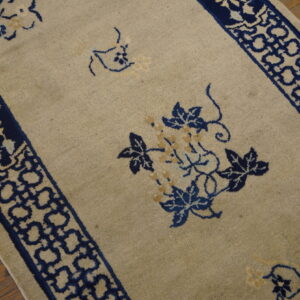 Beige rug with navy blue borders featuring geometric and floral motifs on wood flooring.