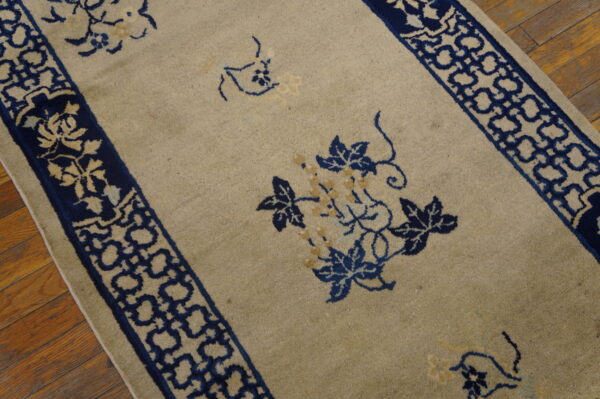 Beige rug with navy blue borders featuring geometric and floral motifs on wood flooring.