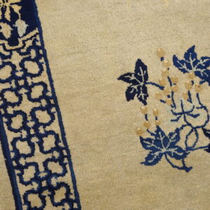 Beige rug detail featuring navy blue floral designs and a repeating border resting on wood floorboards.
