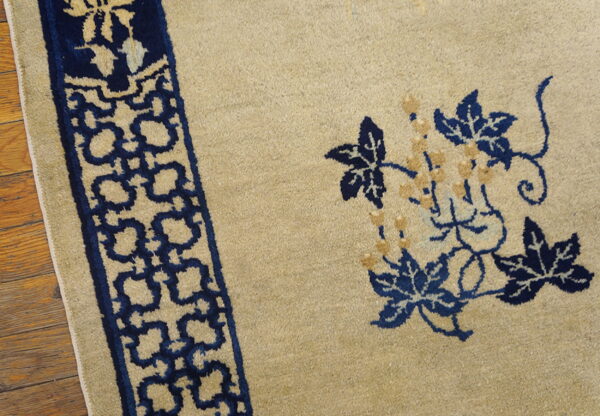 Beige rug detail featuring navy blue floral designs and a repeating border resting on wood floorboards.