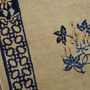 Detail of a tan rug showing navy blue floral vines and a geometric border on wood flooring.