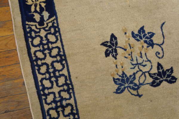 Detail of a tan rug showing navy blue floral vines and a geometric border on wood flooring.