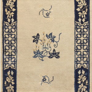 Beige rug with a low pile, a navy blue geometric border, and scattered blue floral designs in the center.