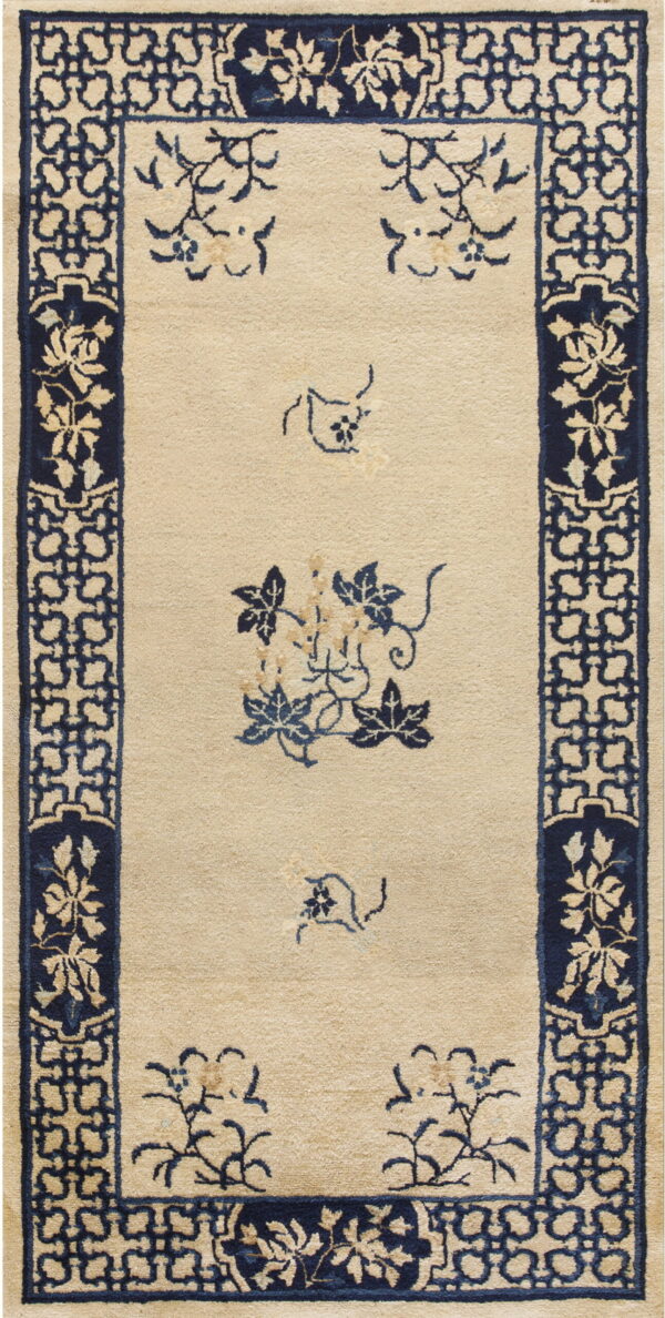 Beige rug with a low pile, a navy blue geometric border, and scattered blue floral designs in the center.