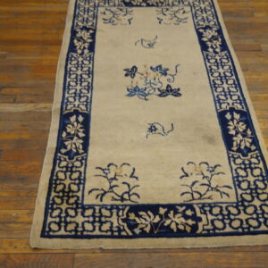 A creamy white runner rug with navy blue geometric borders and sparse floral motifs rests on hardwood floor.