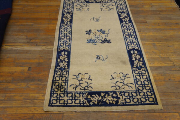 A creamy white runner rug with navy blue geometric borders and sparse floral motifs rests on hardwood floor.