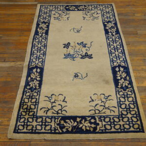 Rectangular rug with a cream field and dark blue stylized floral and geometric borders on distressed wood.