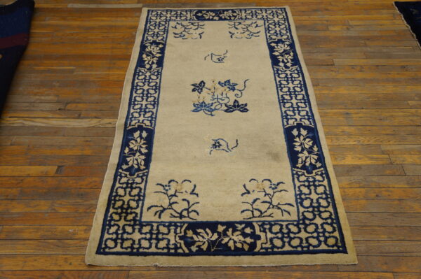 Rectangular rug with a cream field and dark blue stylized floral and geometric borders on distressed wood.