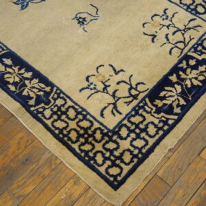 Cream rug with sparse blue florals and complex borders rests on rustic, distressed wood planks.