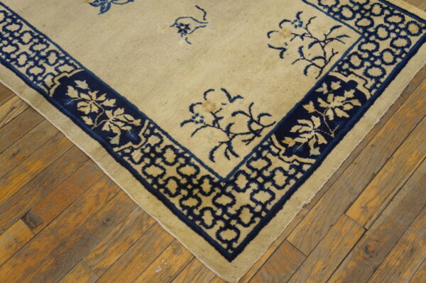 Cream rug with sparse blue florals and complex borders rests on rustic, distressed wood planks.