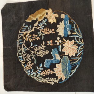 Square black rug with a central medallion of blue, cream, and salmon flowers on white floor.