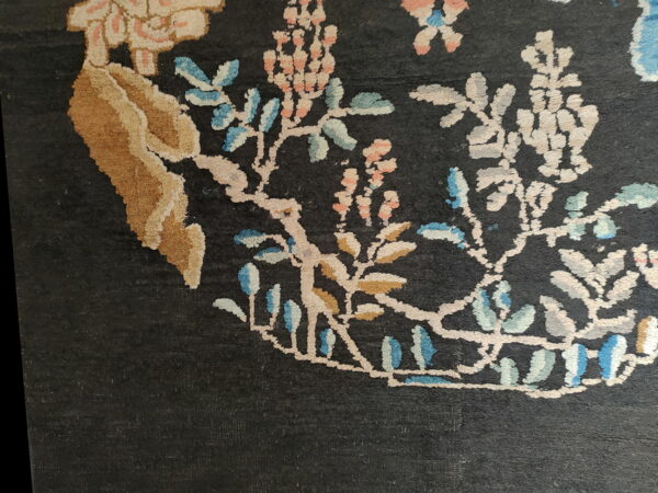 Dark field rug detail showing ornate vines and stylized flowers in cream, tan, pink, and light blue.