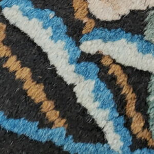 A plush black rug featuring a vibrant floral pattern in blue, gold, cream, and pink next to a dark flatweave texture.