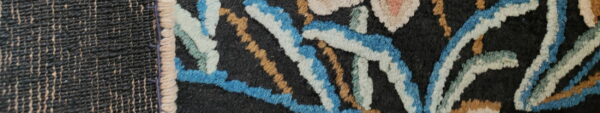 A plush black rug featuring a vibrant floral pattern in blue, gold, cream, and pink next to a dark flatweave texture.