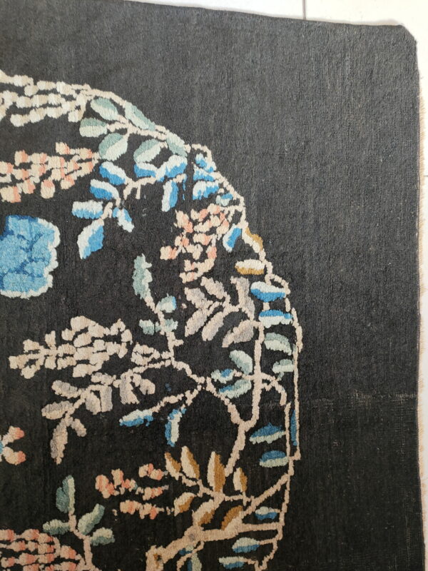 Black rug with a low pile features stylized branches, blue leaves, and pink floral details.