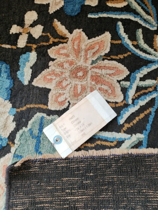 A label rests on a dark, high-pile rug with stylized flowers in peach, blue, and cream colors.