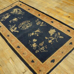 Navy blue rug with beige floral patterns and a wide terracotta border rests on worn wooden floors.