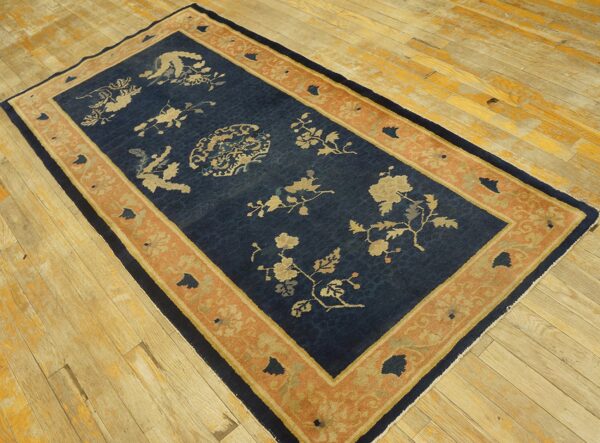 Navy blue rug with beige floral patterns and a wide terracotta border rests on worn wooden floors.