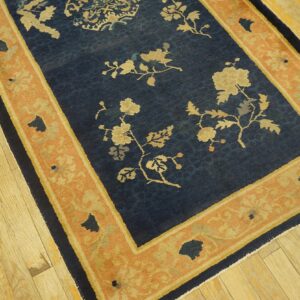 Low-pile navy rug with tan floral patterns and a terracotta border rests on distressed wood flooring.
