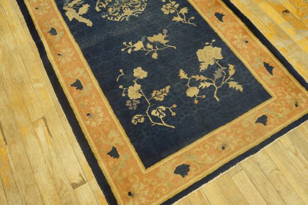 Low-pile navy rug with tan floral patterns and a terracotta border rests on distressed wood flooring.