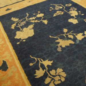 Dark blue rug with tan floral vines and an orange border rests on light wood planks.
