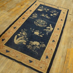 Dark blue rug with light floral patterns and a peach border lies on heavily textured wood planks.