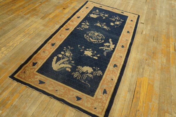 Dark blue rug with light floral patterns and a peach border lies on heavily textured wood planks.