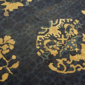 Close-up of a low pile rug featuring golden yellow floral motifs on a textured dark blue background.