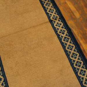 Close-up view of a gold rug featuring dark blue patterned borders on rustic wood floors.