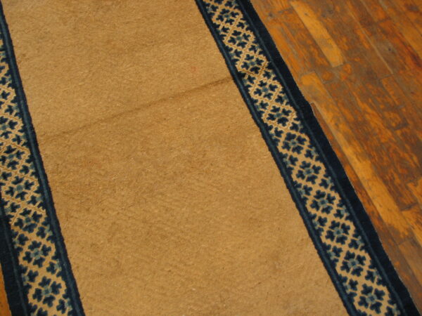 Close-up view of a gold rug featuring dark blue patterned borders on rustic wood floors.