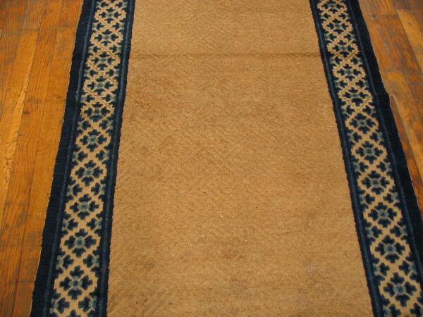 A tan runner with a geometric blue and beige border is laid on distressed wooden flooring.