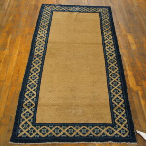 Long tan runner rug with dark blue lattice border on distressed hardwood flooring.