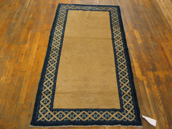 Long tan runner rug with dark blue lattice border on distressed hardwood flooring.