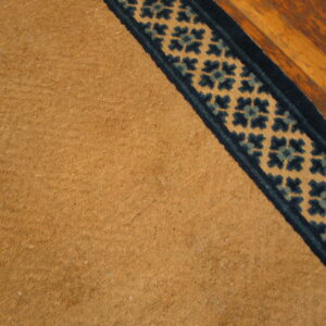 Camel rug with a dark blue and teal patterned border lying on distressed wood planks.