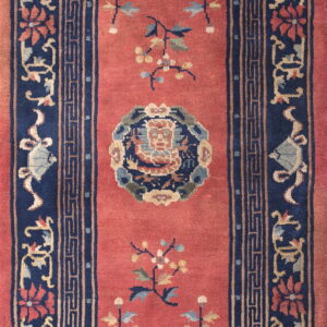 Rust-red runner rug with a navy border displaying ornate floral designs and a Greek key pattern.